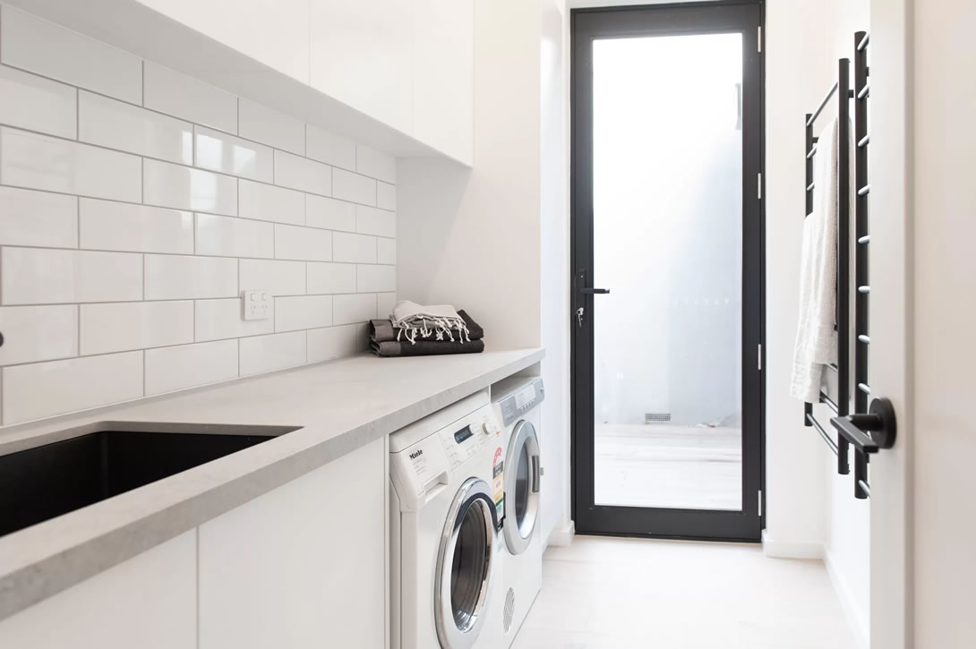 Laundry with white cabinetry with black sink and heating rails